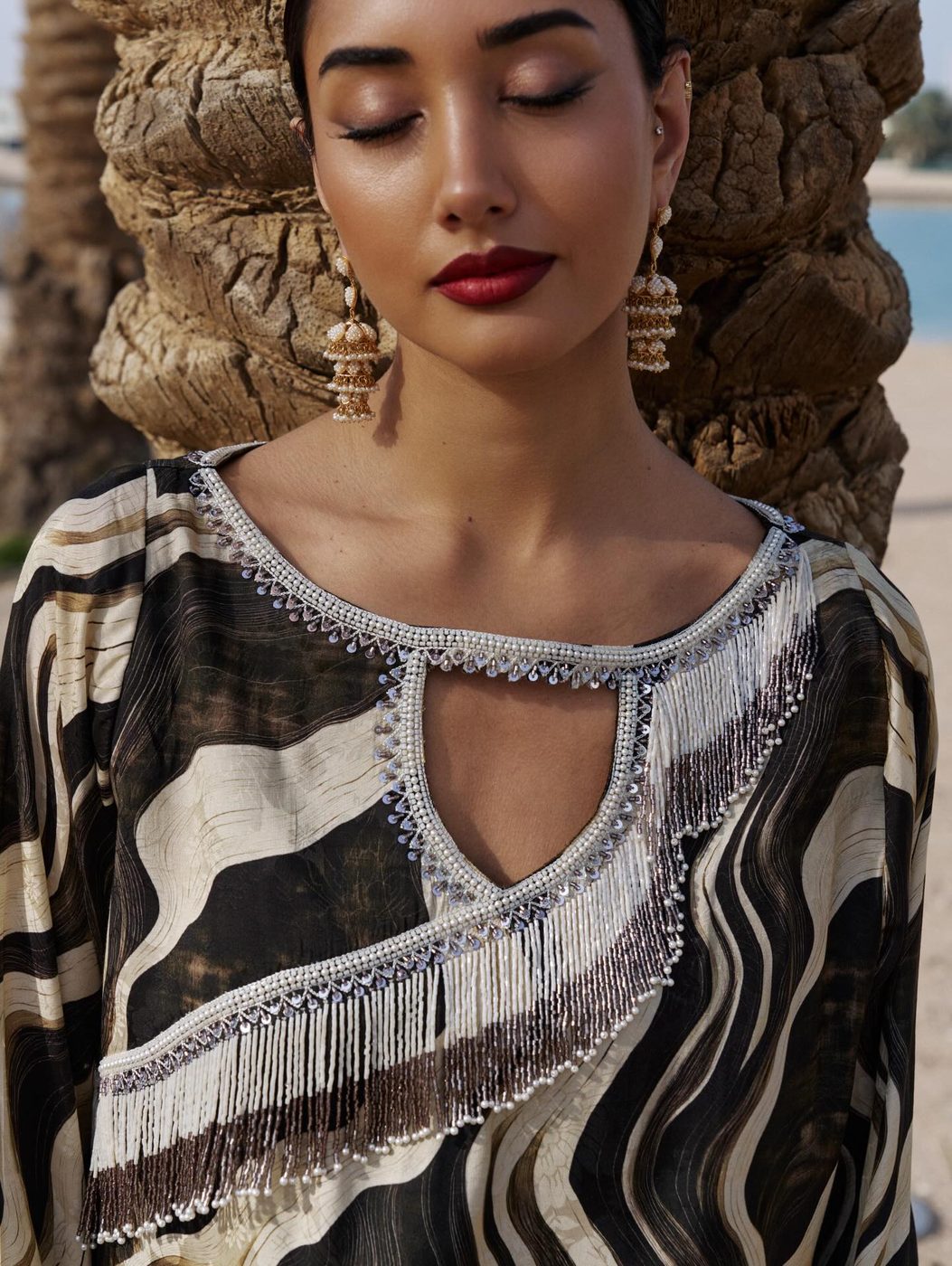 Model in a patterned Mash abaya with a fringed neckline, eyes closed