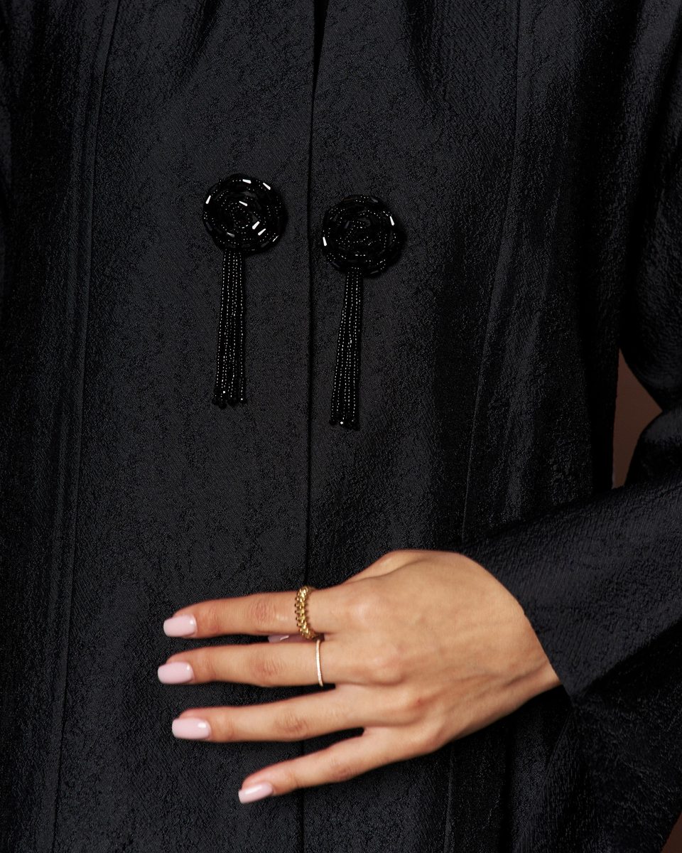 Close-up of tassel buttons on a black textured abaya